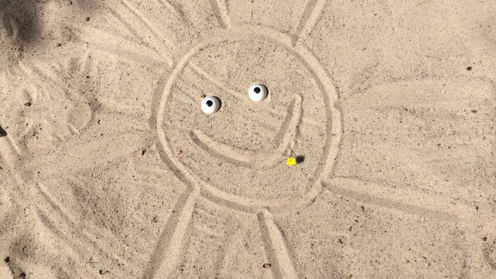 Das Augenpaar liegt im Sand. Eine Sonne ist um die Augen in den Sand gezeichnet.