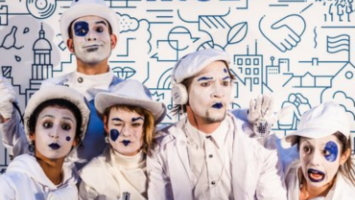 Pantomime-Künstler:innen und Kommunikator:innen stehen vor einer weißen Leinwand mit dem blauem Schriftzug "fair.kiez.". Sie sind weiß gekleidet und geschminkt, mit blauen Akzenten.