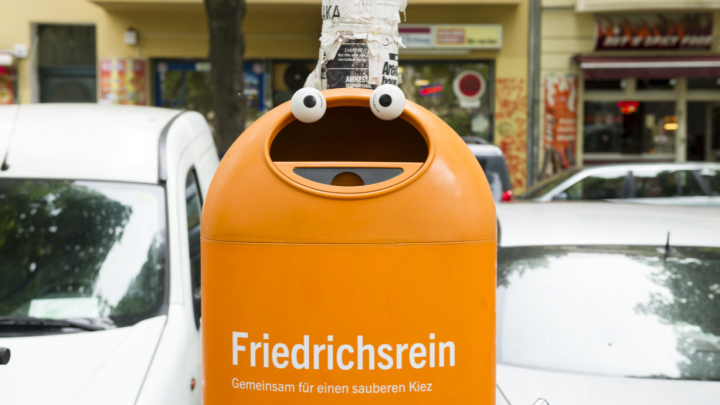 Ein orangener Mülleimer mit einem aufgeklebten Augenpaar und dem Schriftzug "Friedrichsrein - Gemeinsam für einen sauberen Kiez"